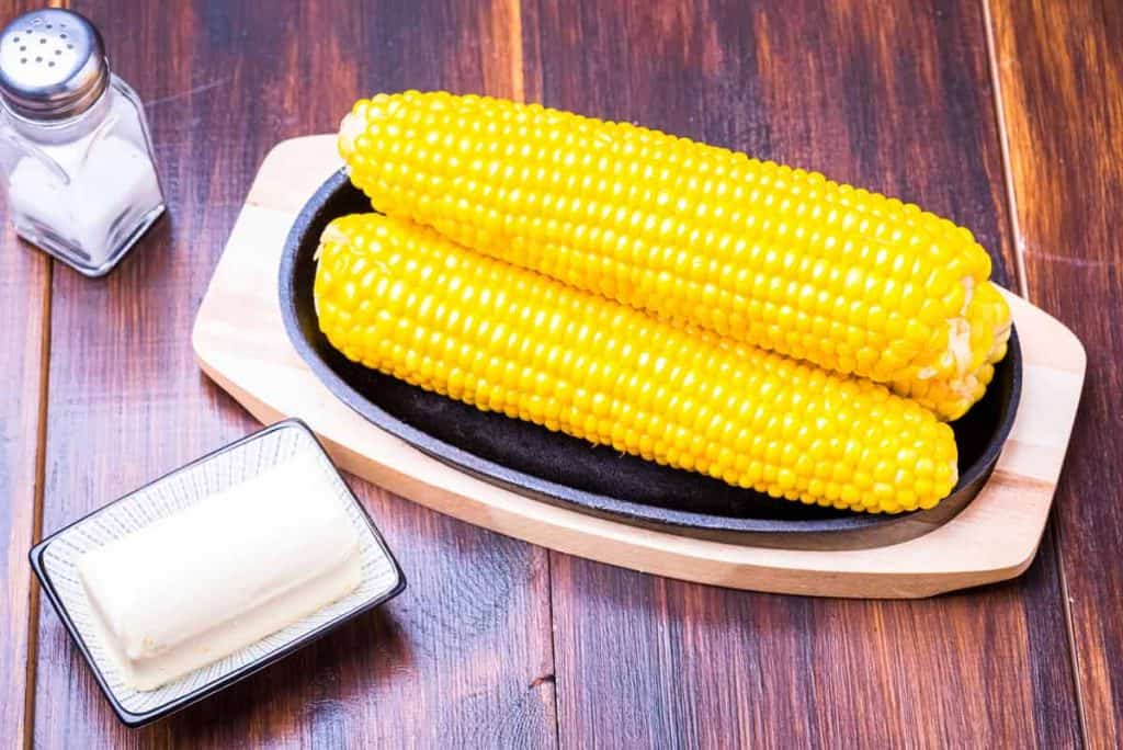 corn on the cob, butter, and salt shaker on a wooden table
