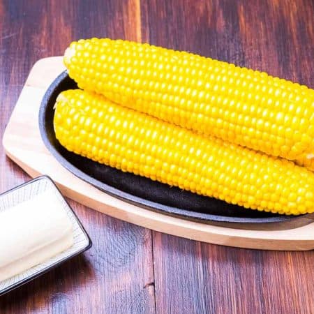 corn on the cob, butter, and salt shaker on a wooden table