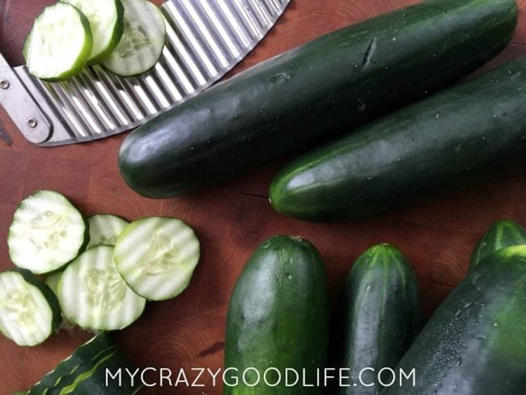 whole cucumbers, sliced cucumbers, and a crinkle cut blade on a dark countertop