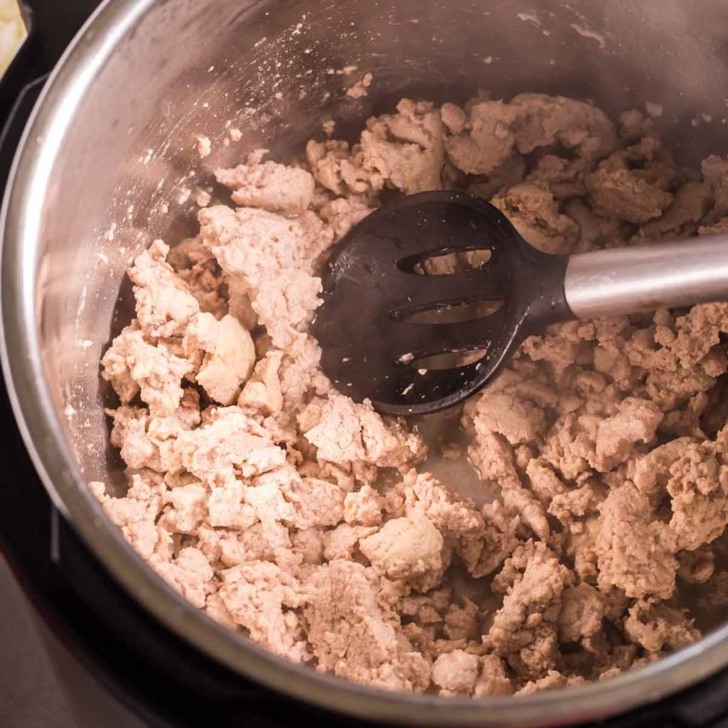 Open Instant Pot on saute mode, with ground turkey and a black spoon with a silver handle stirring the meat. 