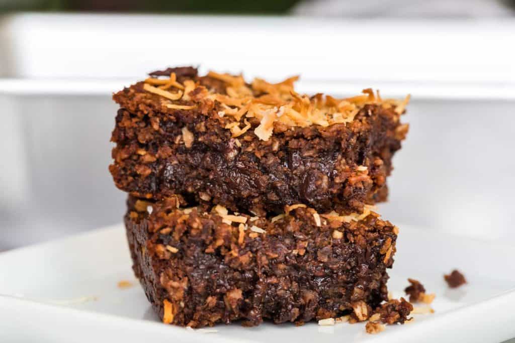 Two stacked brownies with toasted coconut on top on a white plate. 