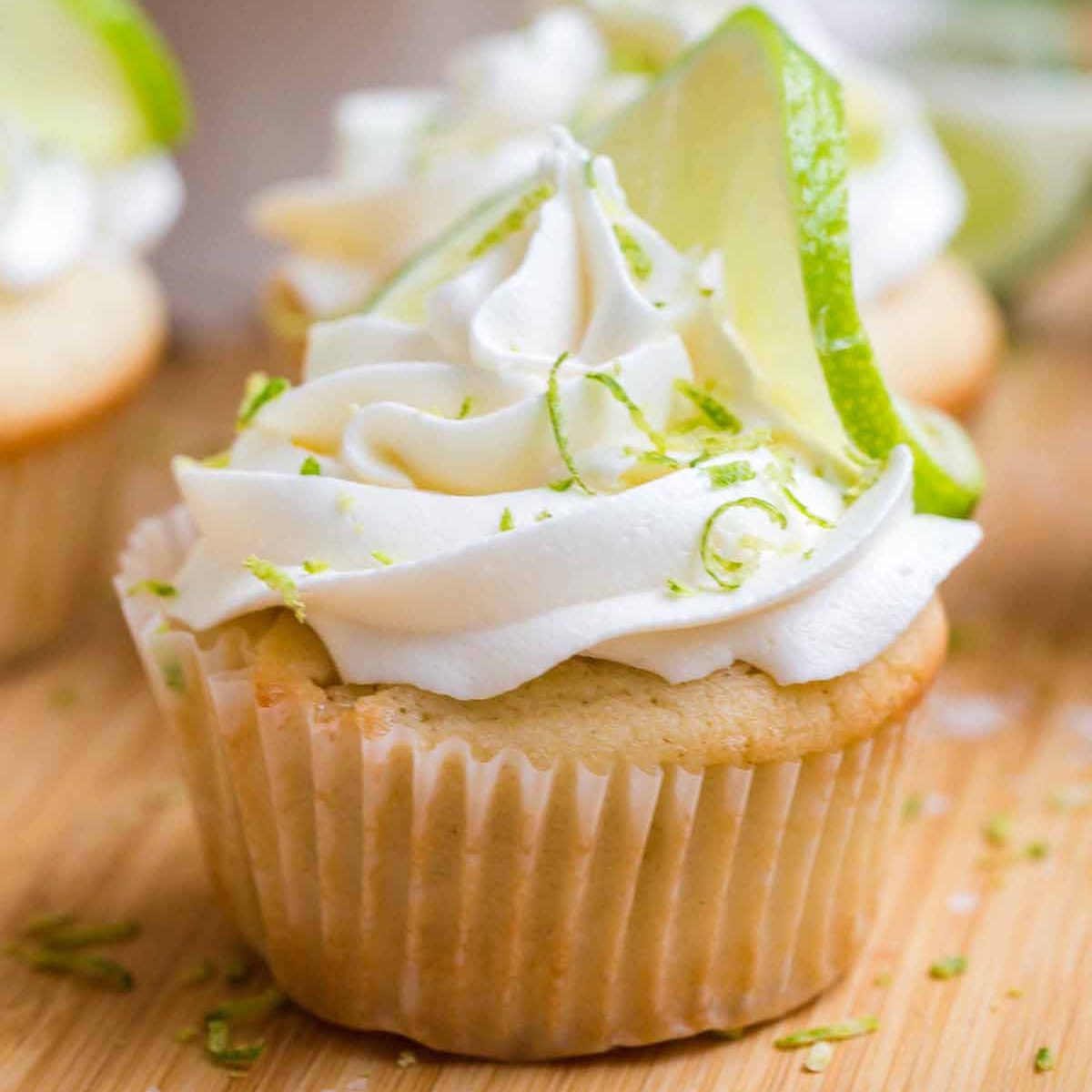 Frosted and garnished margarita cupcake on a wood cutting board.