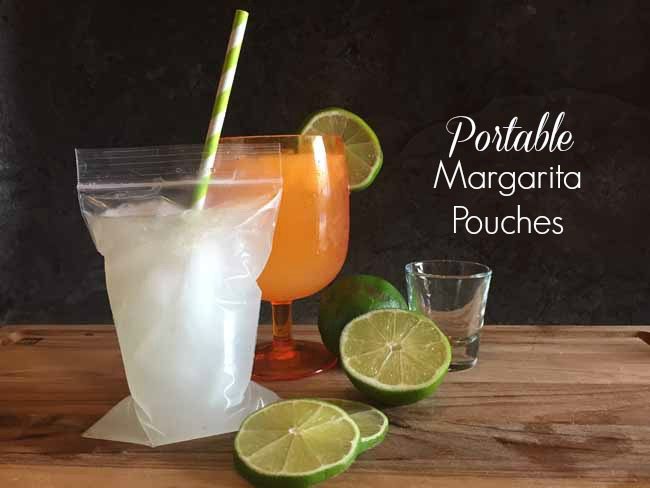 a portable margarita pouch next to an orange plastic cup with a margarita in it. To the side are a shot glass and lime slices.