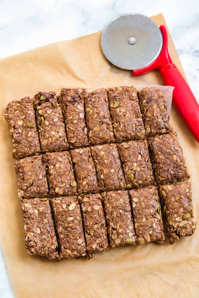 cut homemade granola bars on top of parchment paper with red pizza cutter to the side