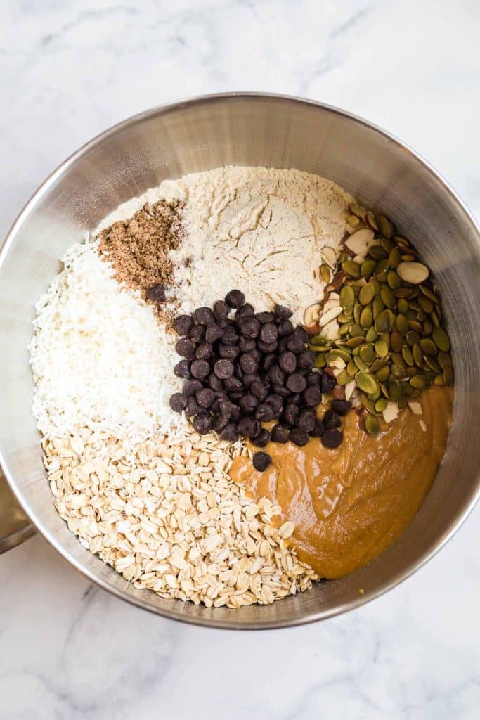 mixing bowl showing oats, peanut butter, honey, coconut flakes, chocolate chips and other add-ins to make granola bars