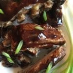 Baby back ribs with BBQ sauce and garnished with sliced green onion.