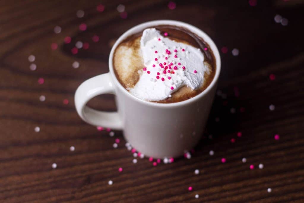 white mug with Boozy Mexican Hot Chocolate, topped with whipped cream and pink sprinkles