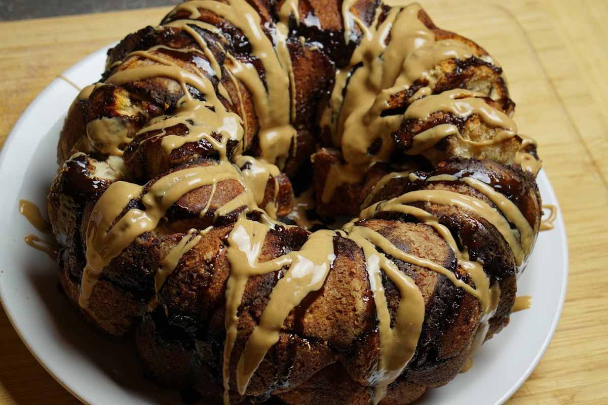 Peanut Butter Cup Monkey Bread in the shape of a bundt on top of a white plate and drizzled with peanut butter and chocolate.