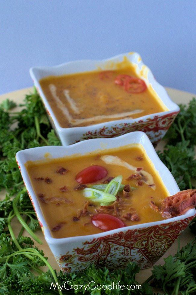two square bowls of butternut squash soup on a plate with salad greens