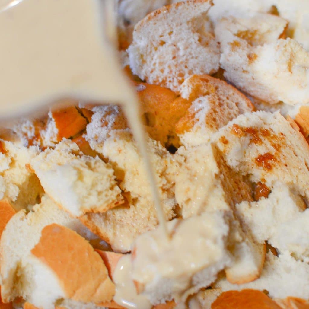 Cubed dinner roll bread with a french toast egg mixture being poured on top.