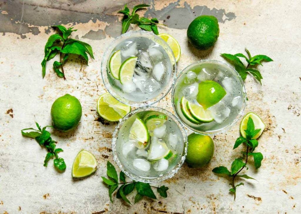 image of three glasses with ice, lime slices, mint and water from above.