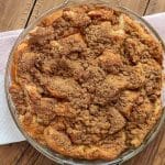 A circular baking dish filled with french toast casserole and topped with a cinnamon strudel, sitting on a folded red and white napkin on a wooden table.