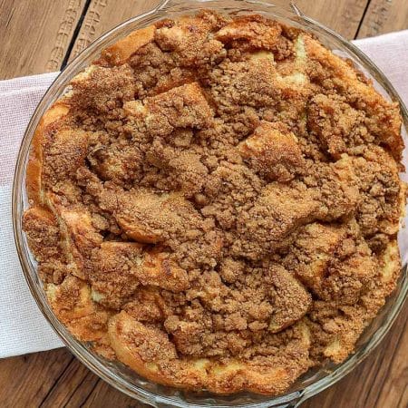 A circular baking dish filled with french toast casserole and topped with a cinnamon strudel, sitting on a folded red and white napkin on a wooden table.