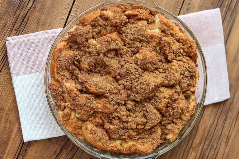 A circular baking dish filled with french toast casserole and topped with a cinnamon strudel, sitting on a folded red and white napkin on a wooden table.