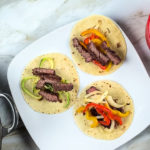 Steak fajitas with flour tortillas on a square white plate.