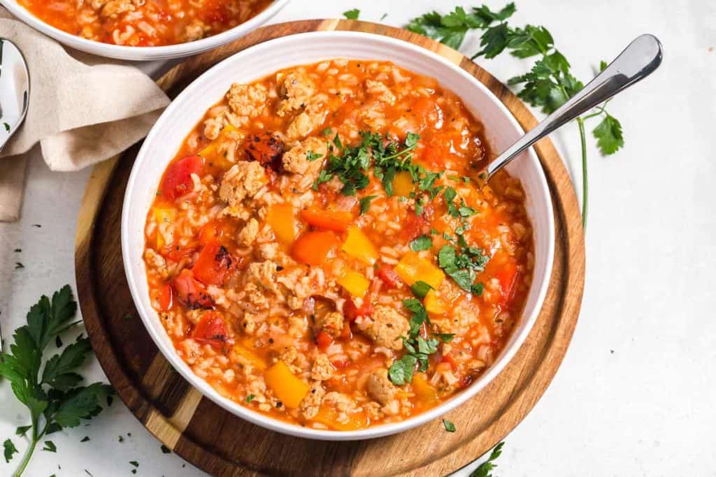 Image of white bowl filled with stuffed pepper soup. The bowl is sitting on a wooden plate on top of a white counter.