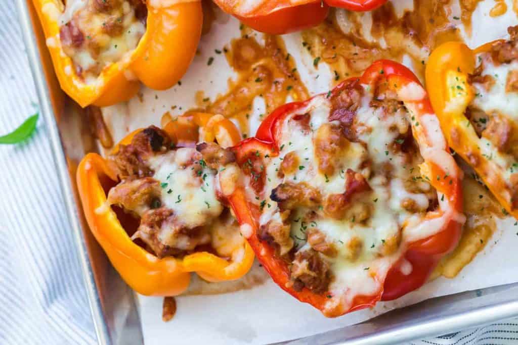 Image of red and orange bell peppers stuffed with pizza-like toppings and topped with melted cheese.