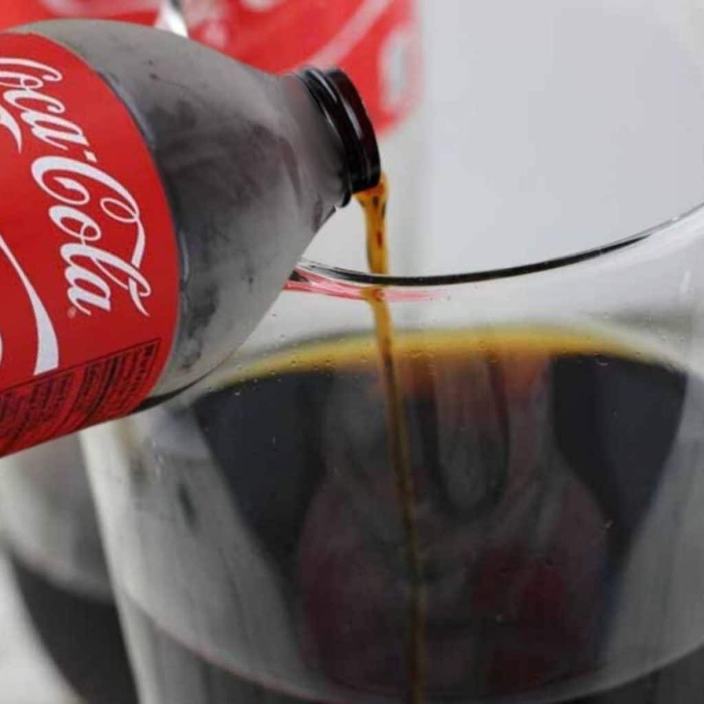 A bottle of coca-cola being poured into a glass.