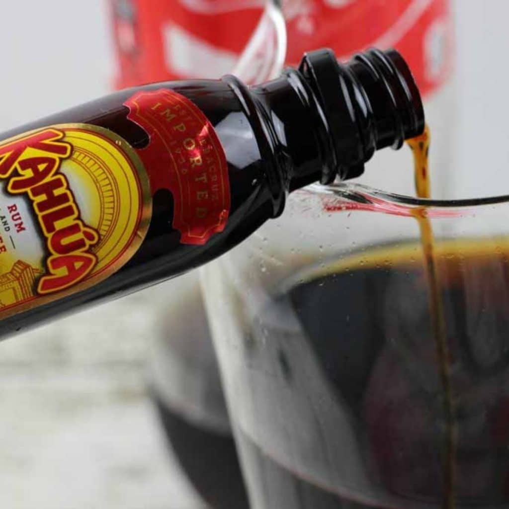 A small bottle of Kahlua being poured into a glass.