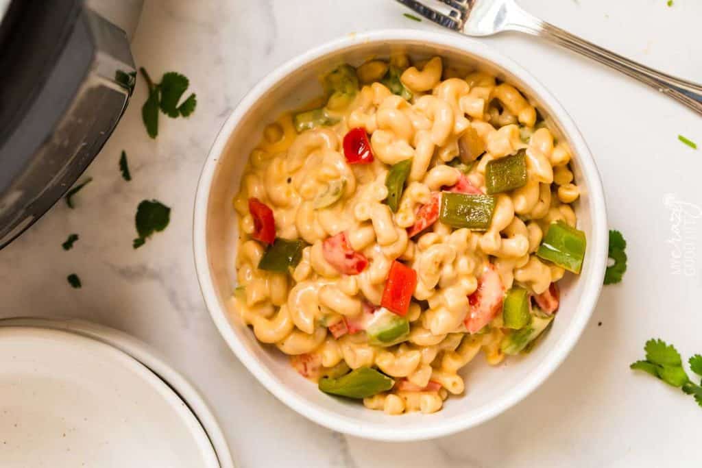 Image of a bowl of macaroni and cheese garnished with bell peppers. The mac and cheese is in a white bowl on top of a white marbled countertop. 