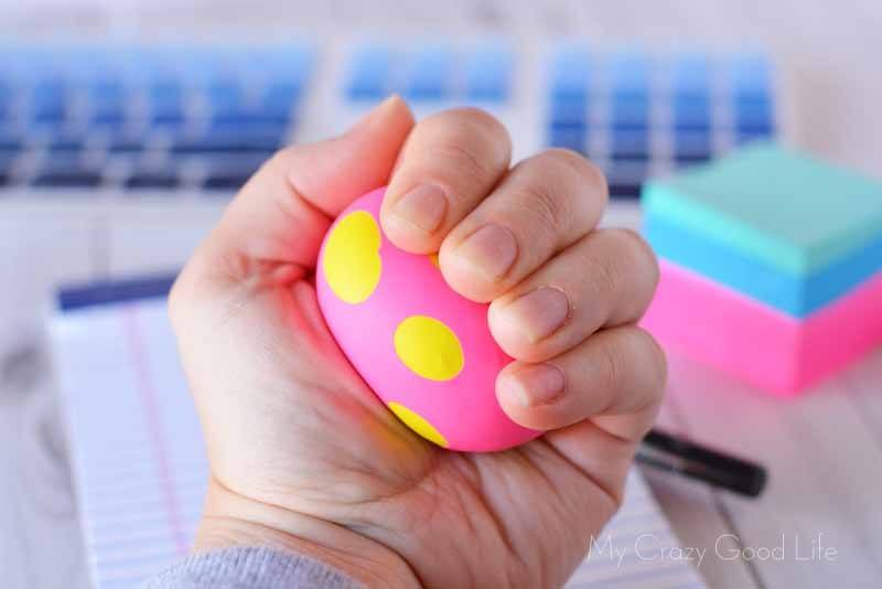 hand squeezing a yellow and pink ball