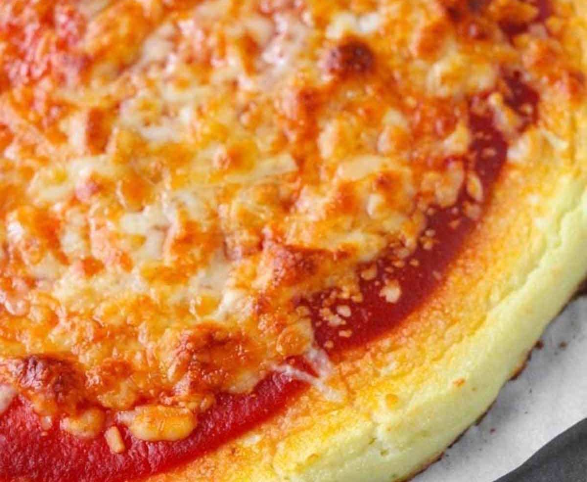 Cooked cauliflower crust pizza with cheese topping on top of a parchment paper lined baking sheet.