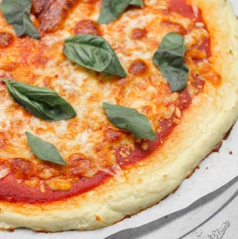 cooked cauliflower pizza with melted cheese and fresh basil on top.