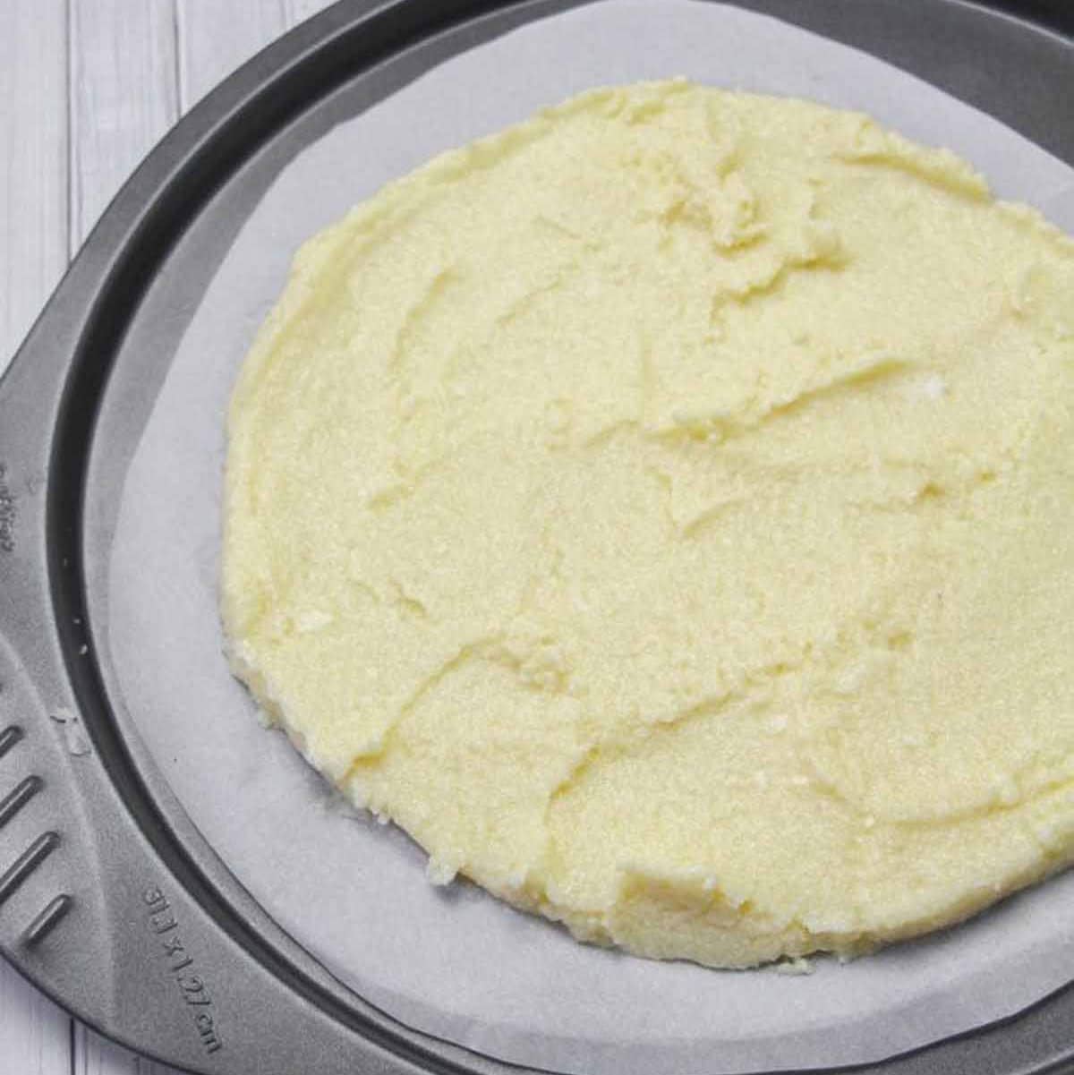 circle shaped cauliflower, cheese, egg mixture on a piece of parchment paper to be cooked for pizza crust.