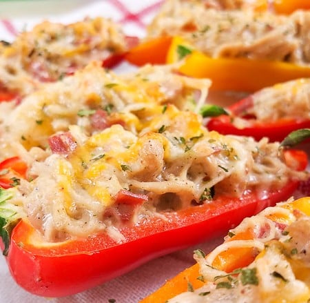 Mini bell peppers cut in half and filled with crack chicken and cheese. There is a red and white checkered napkin under the peppers.