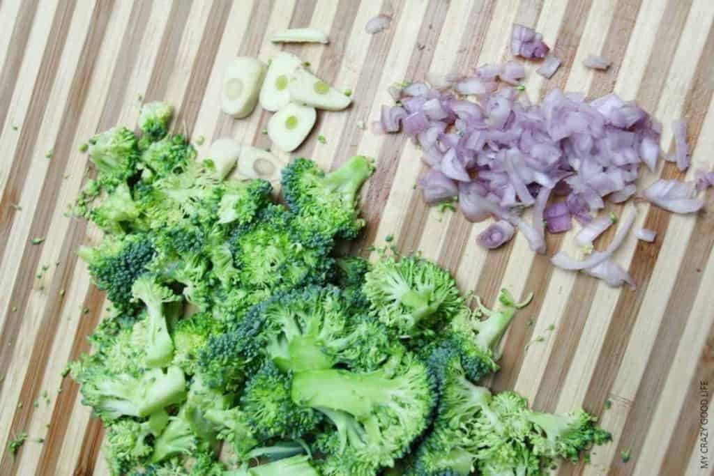 chopped broccoli, shallots, and garlic on a wooden cutting board