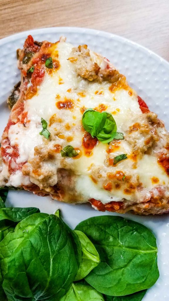 large slice of lasagna on white plate with spinach