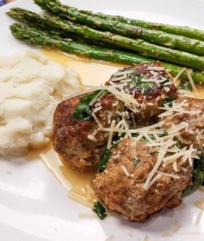 swedish meatballs on a white plate with asparagus and potatoes