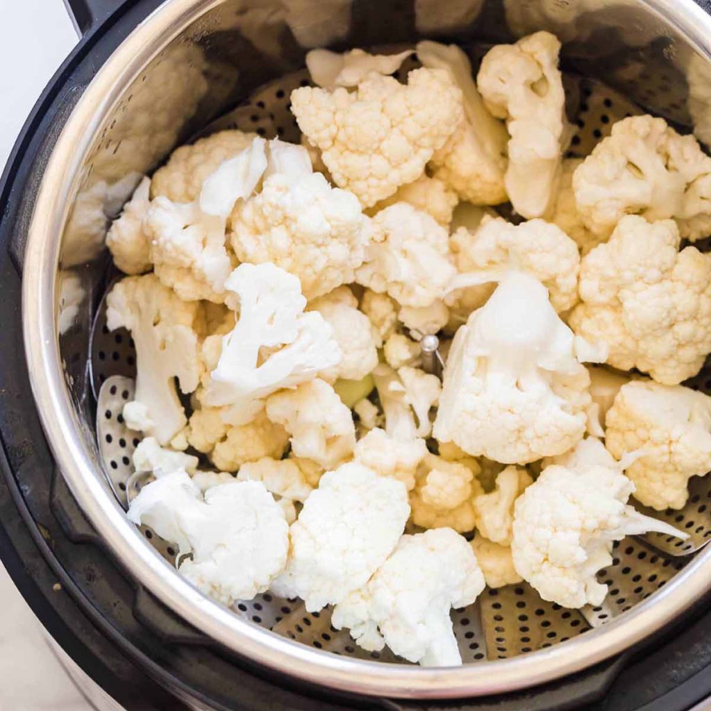 raw cauliflower florets inside of the instant pot, on top of a steaming basket