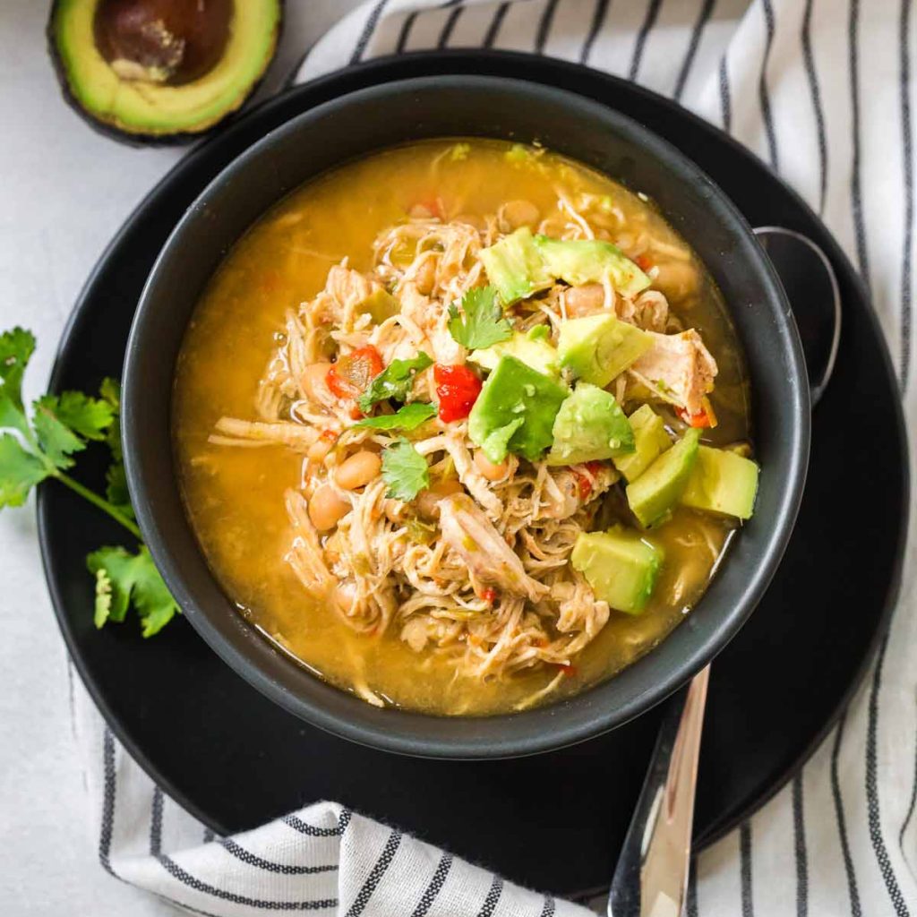 black bowl filled with White Chicken Chili and topped with avocado and cilantro