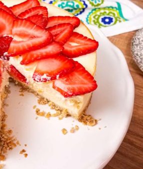white plate with cheesecake, strawberries on top