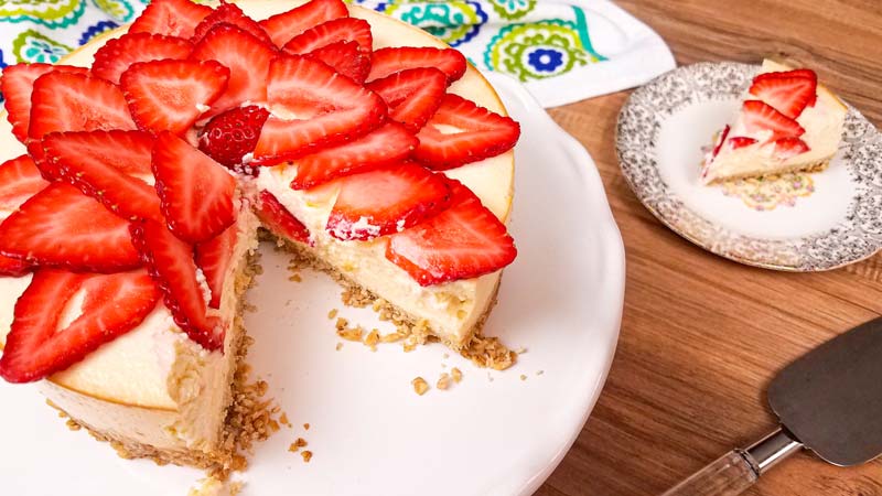white plate with cheesecake, strawberries on top