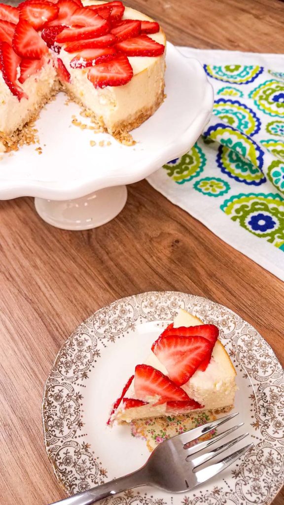 slice of cheesecake on plate with fork, with the rest of the cheesecake on a serving platter in the background
