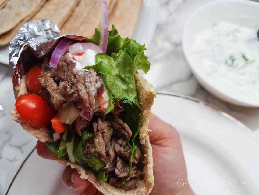 Beef gyro in a hand being held up to show the open side which has meat, vegetables, and sauce inside.