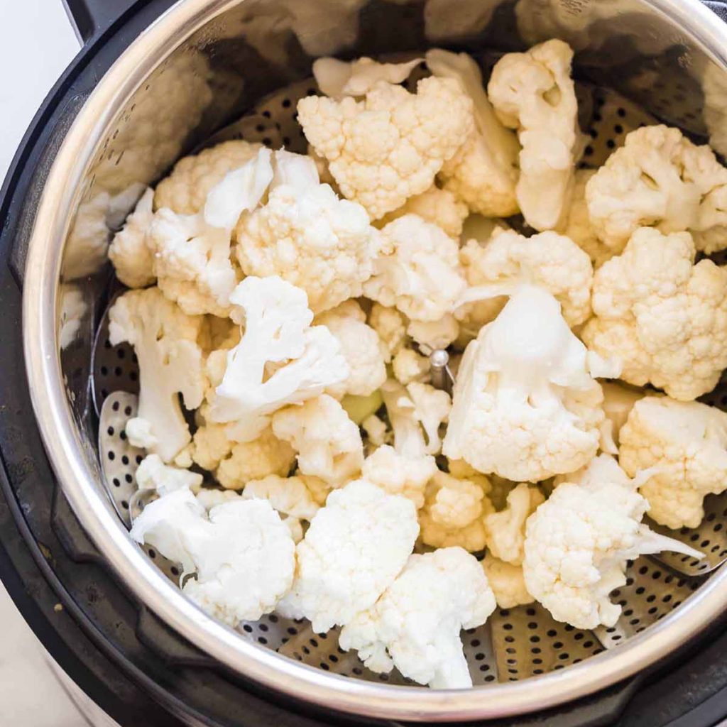 raw cauliflower florets inside of the instant pot, on top of a steaming basket