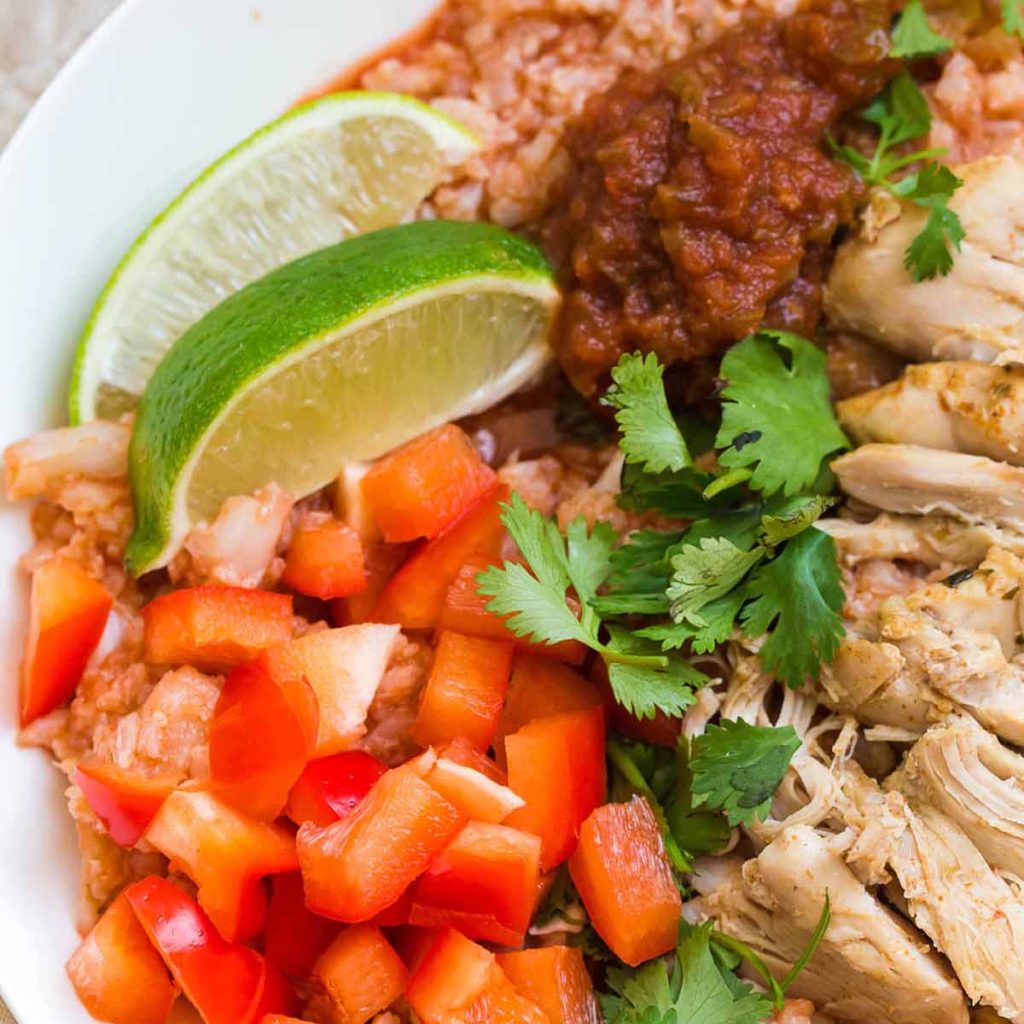 close up of white bowl with spanish cauliflower rice, shredded chicken thighs, fresh tomatoes, and cilantro in it