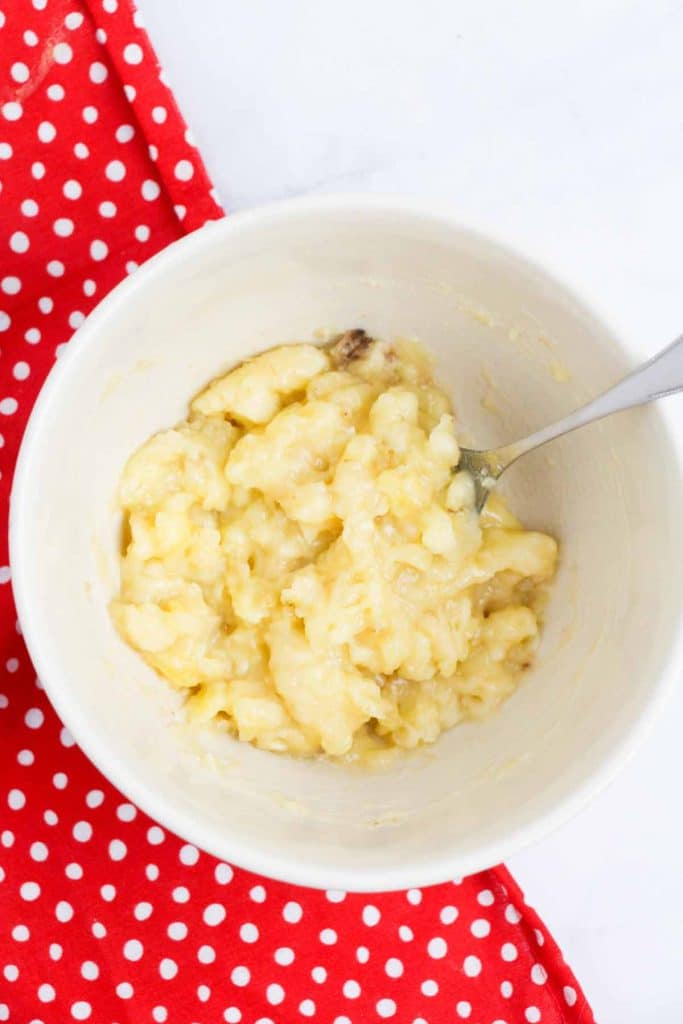 mashed bananas in a white bowl with a red and white polka dot towel underneath