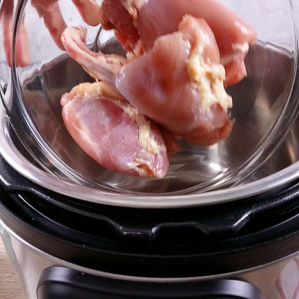 Raw chicken thighs being dumped into an instant pot.