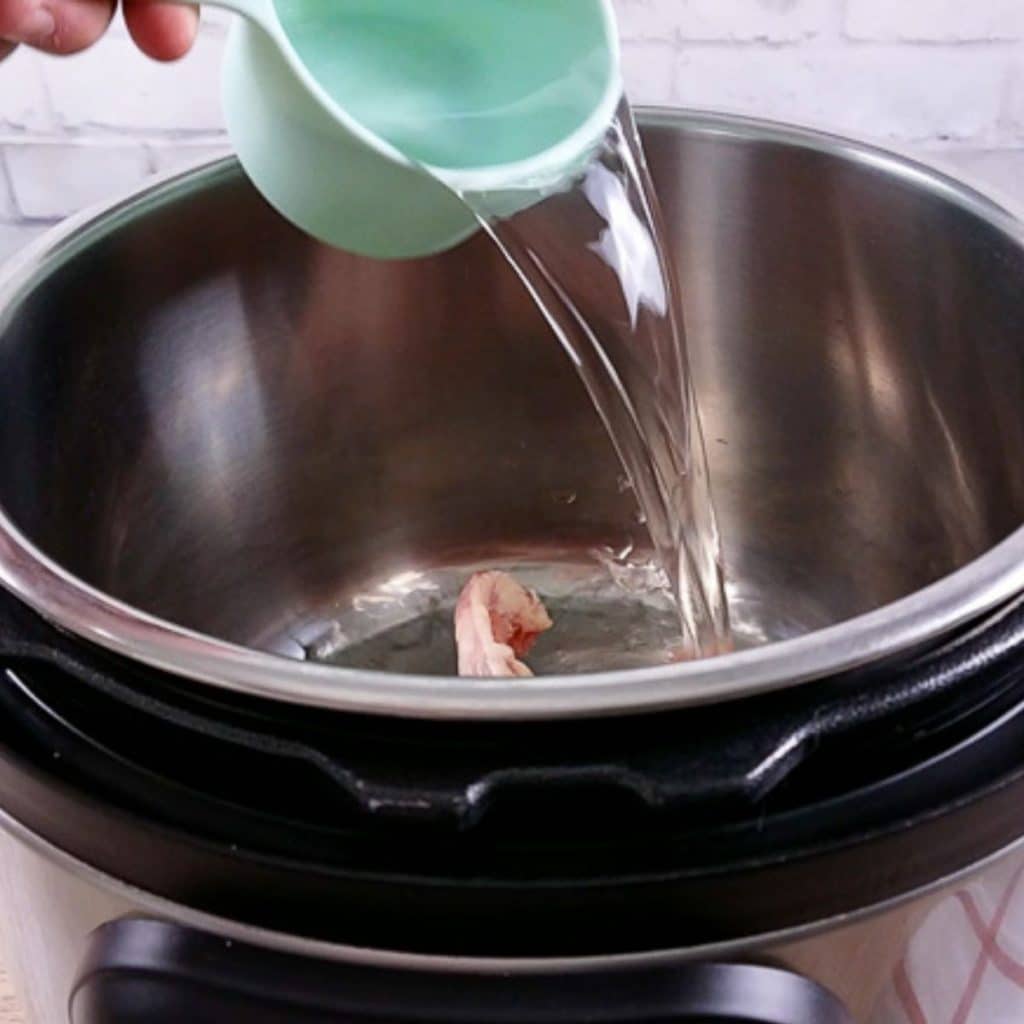 A blue measuring cup pouring water into an instant pot.