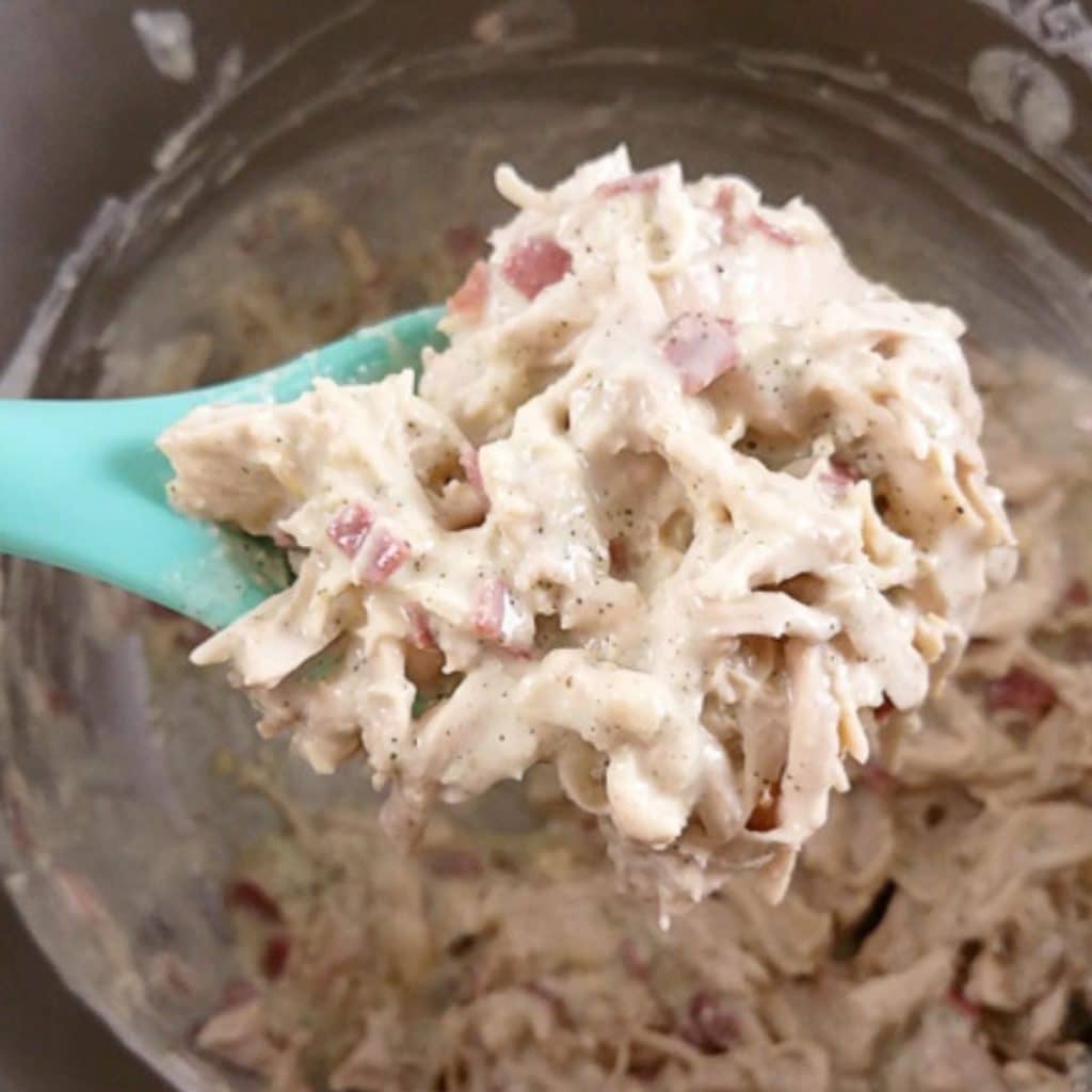 A blue spoon scooping out a spoonful of creamy crack chicken.