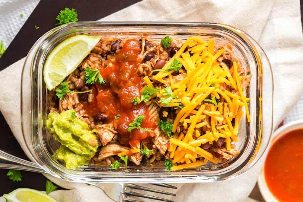Weight Watchers Burrito Bowl in a glass meal prep container. The bowl is garnished with a wedge of lime, guacamole, cheese and salsa.