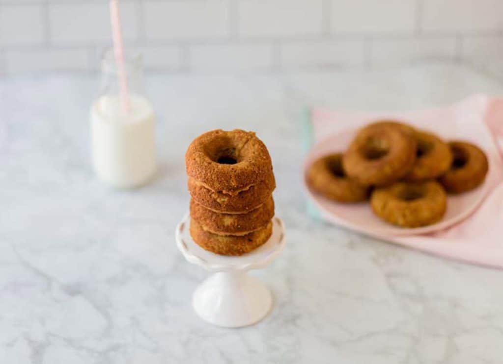 stack of donut in front with milk and tray of donuts in background