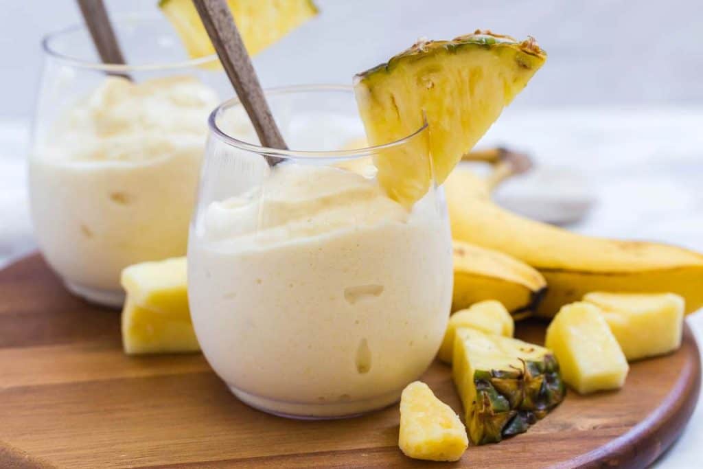 Two dole whips in clear glass with pineapple garnish on the cup and around the base.