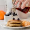 hand pouring syrup onto stack of pancakes