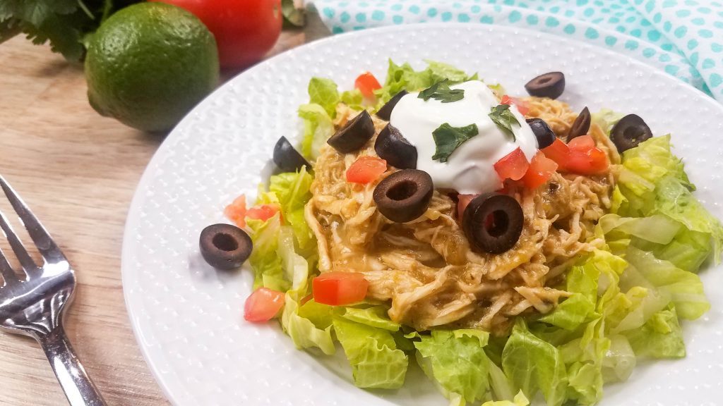 chicken on top of a bed of lettuce with greek yogurt and olives on white plate