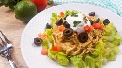 green chili chicken on top of a bed of lettuce with greek yogurt and olives on white plate